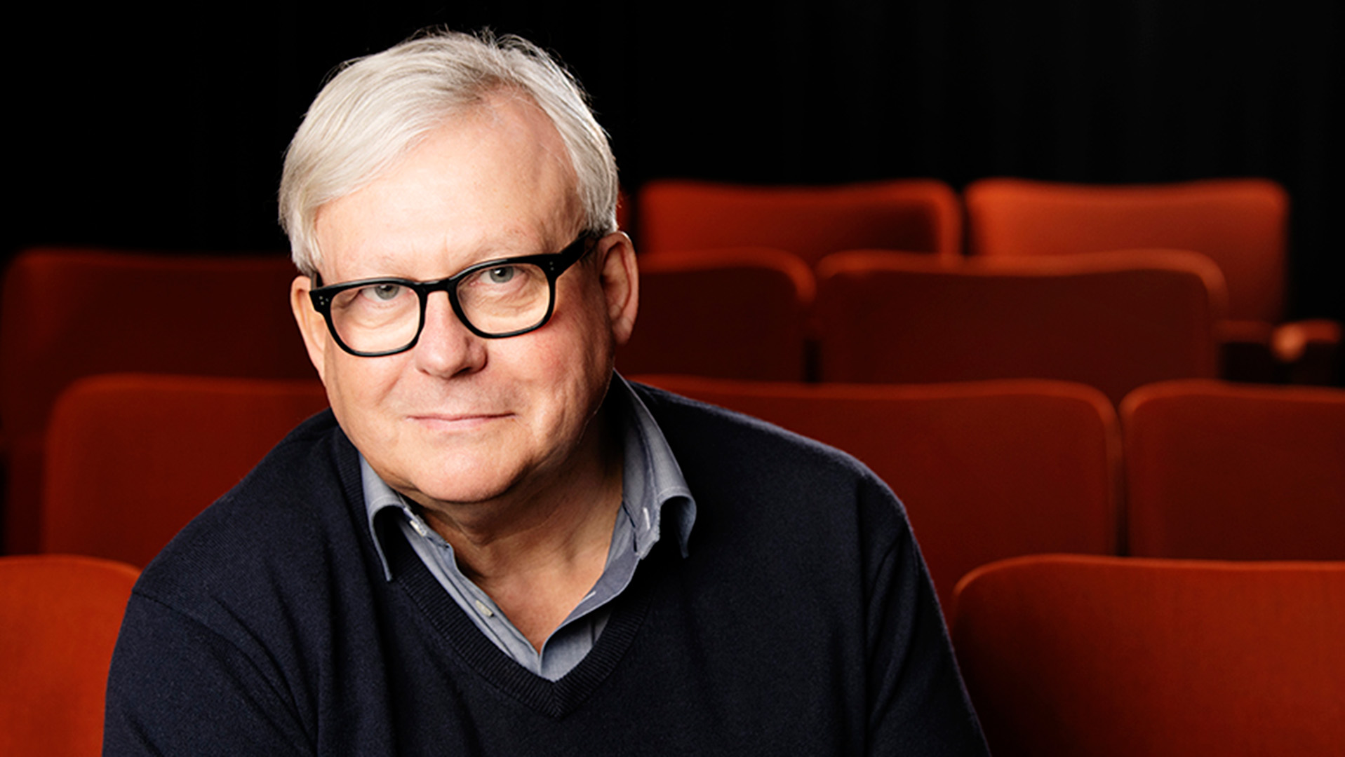 Tomas Eskilsson är i övre medelåldern. Han har grått hår, bär glasögon med svarta bågar och är klädd i en svart v-ringad tröja med en grå skjorta under. Han sitter i en biosalong, de röda sätena syns runt honom.