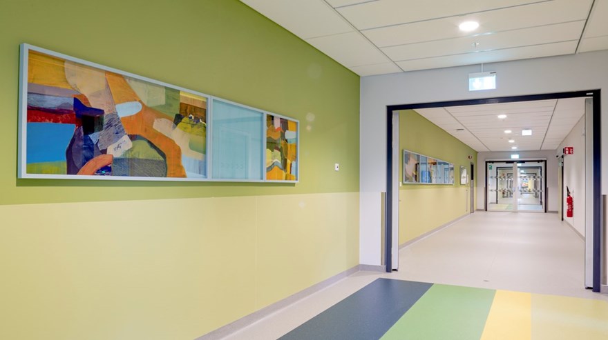 Målningar placerade på en gulgrön vägg i en korridor