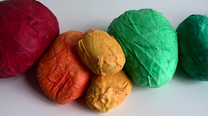 Stenar i olika storlekar inlindade i tygremsor i olika färger. Från vänster röd, orange, två gula stenar och två gröna längst till höger