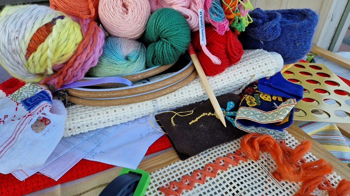 Garner i olika färger ligger på ett bord. En trästicka syns samt ett påbörjat broderi i orange garn.