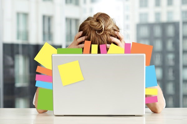 Kvinna som vilar huvudet i händerna bakom laptop fylld av post-it lappar