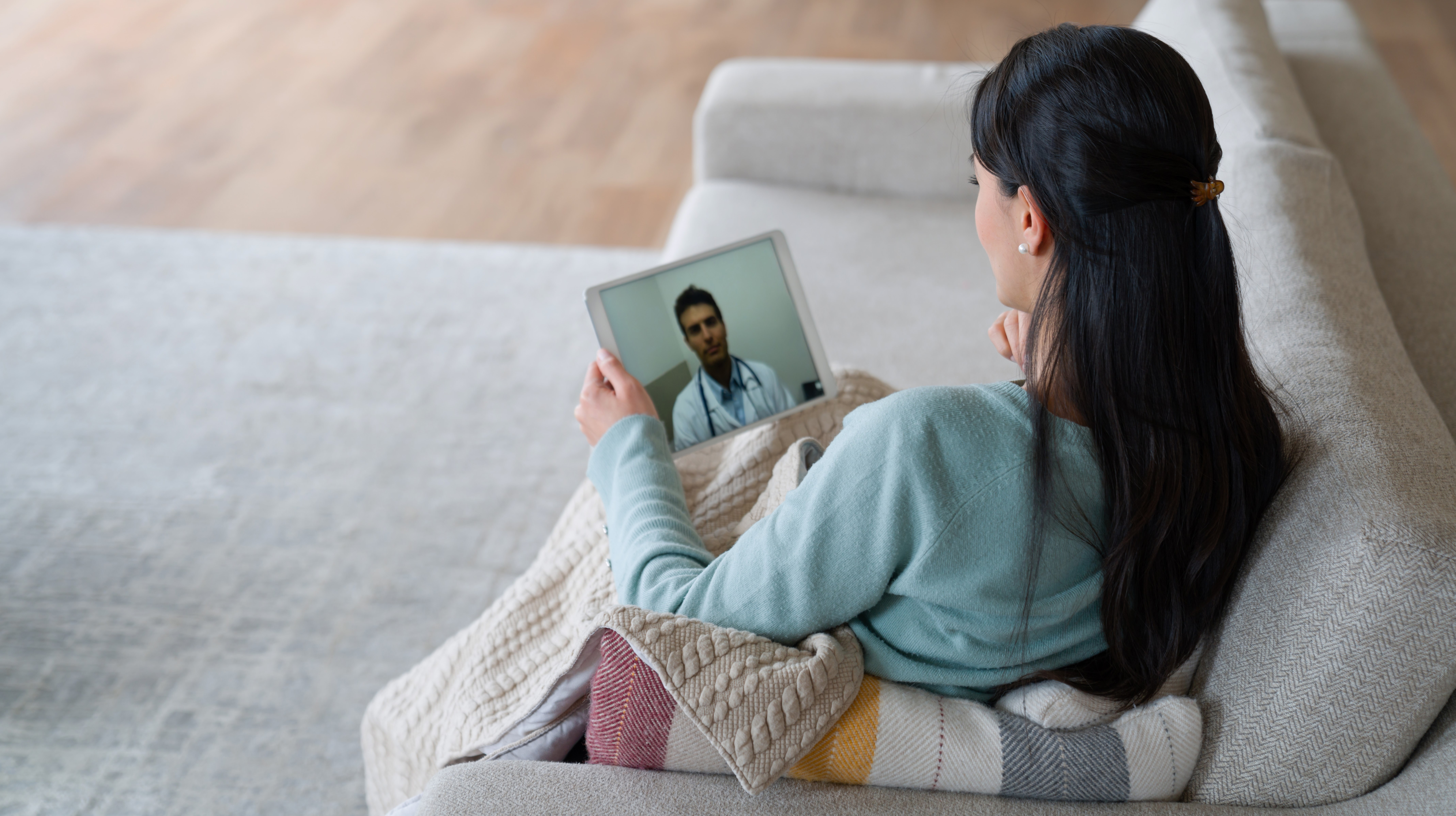 Kvinna som får stöd av läkare via Ipad, sittande i soffa