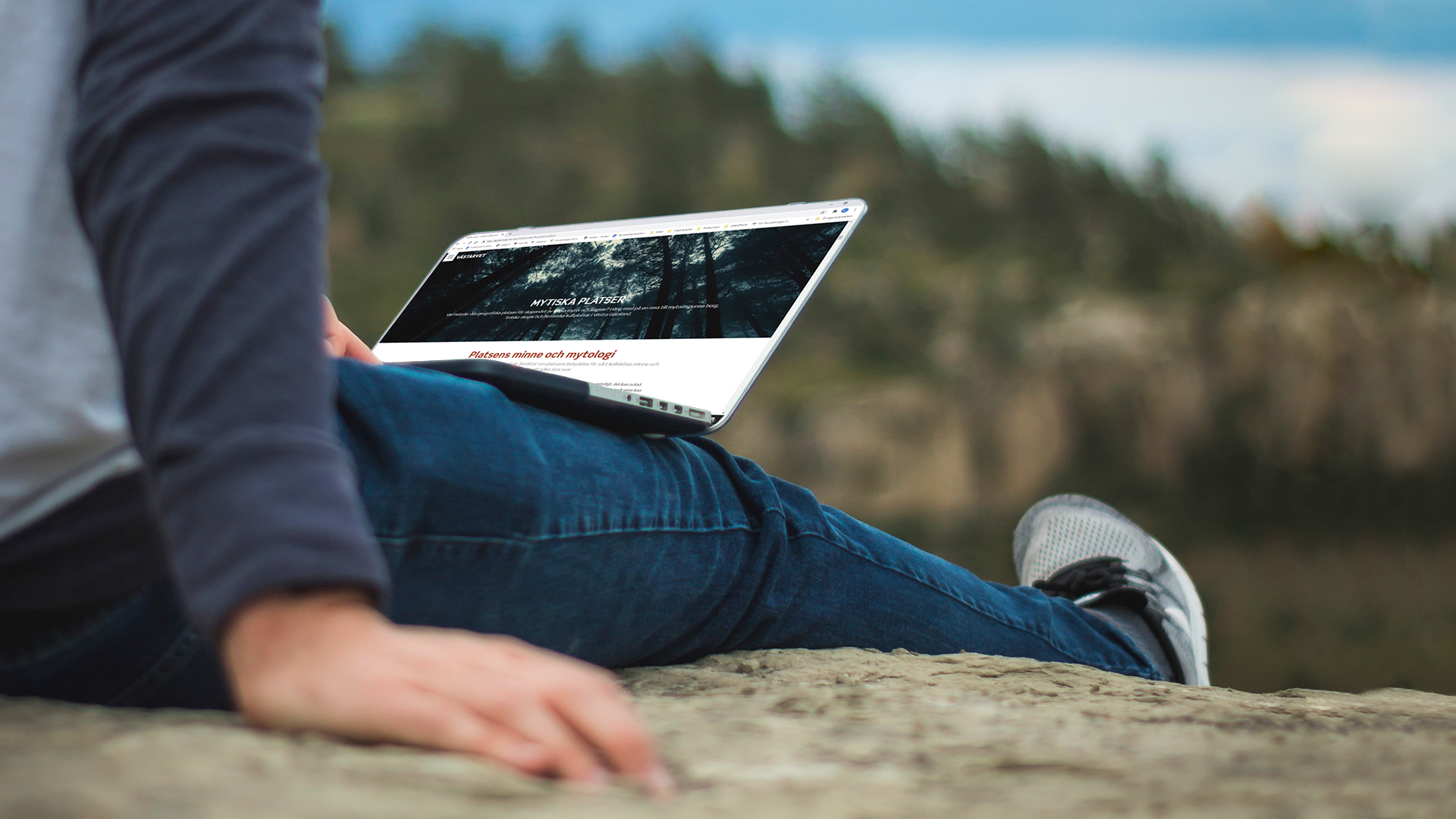 Ett barn sitter på en berghäll med en dator i sitt knä.