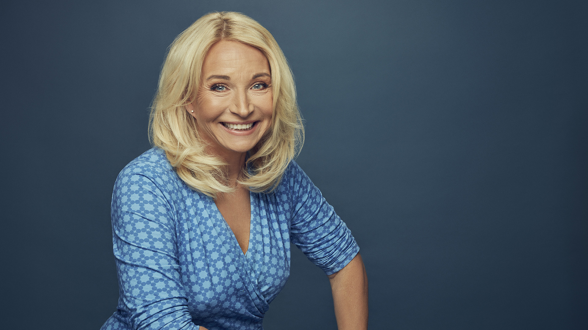 Martina Haag är i medelåldern. Hon har blont lång hår och blå ögon. Hon är klädd i en blåmönstrad omlottklänning och ler stort mot fotografen. Bilden är tagen inomhus. gissningsvis  i en fotostudio.