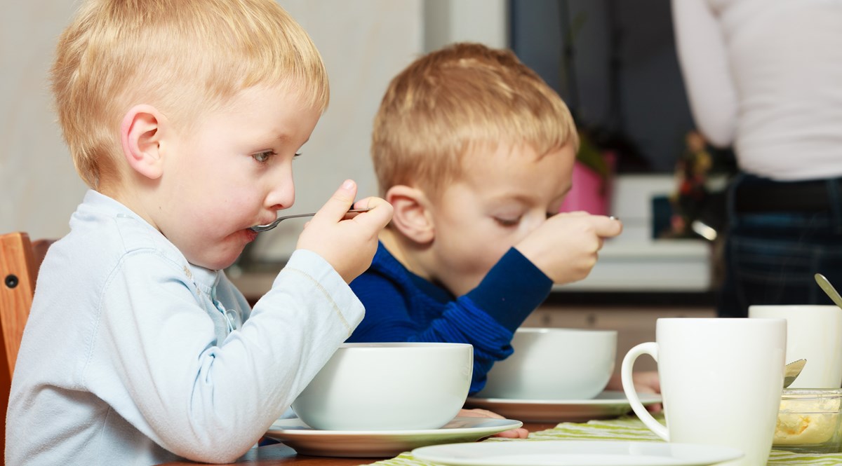 Två små barn äter frukost i djupa skålar