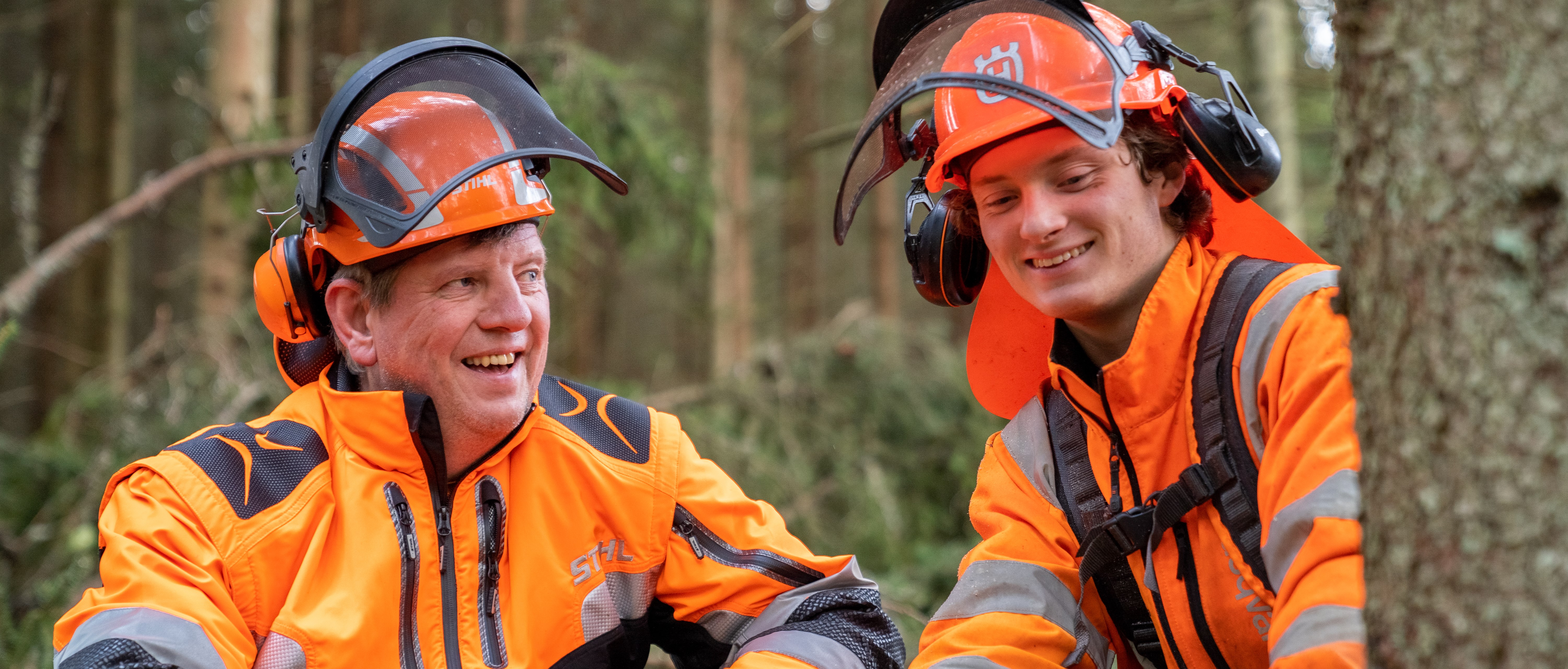 En elev och lärare i skyddskläder jobbar i skogen