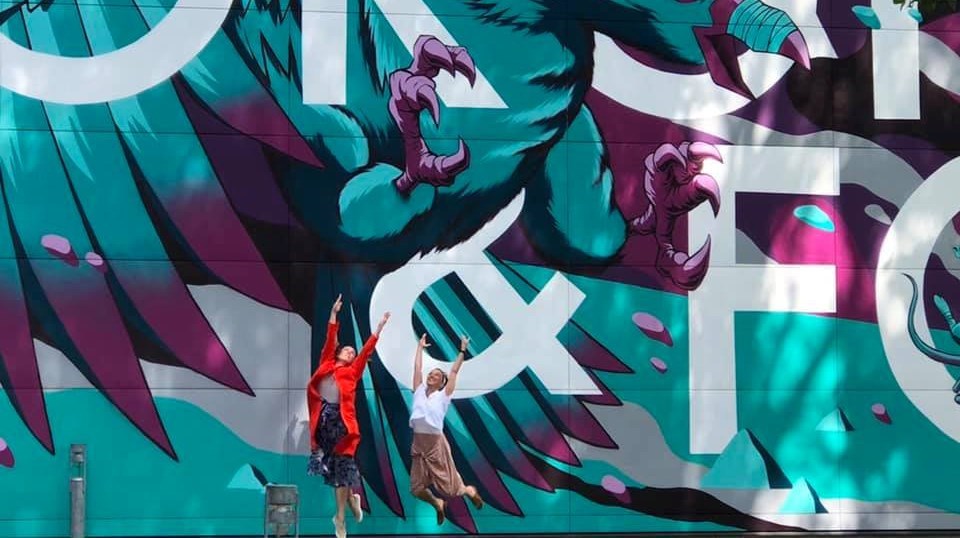 Två personer som hoppar framför en graffitivägg