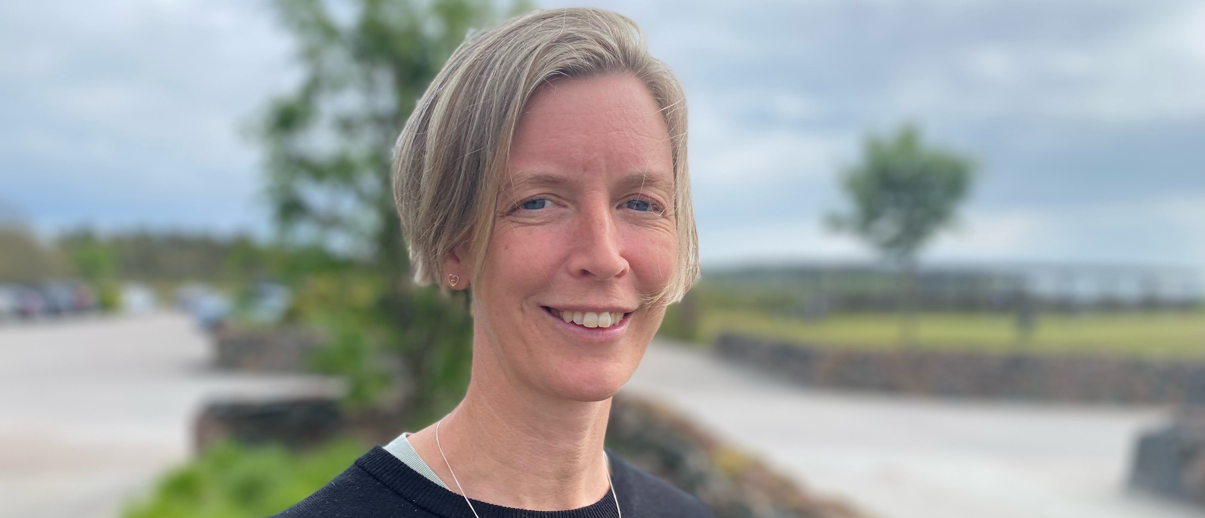 Katarina Nyström står utomhus, håret blåser och himlen är blå.