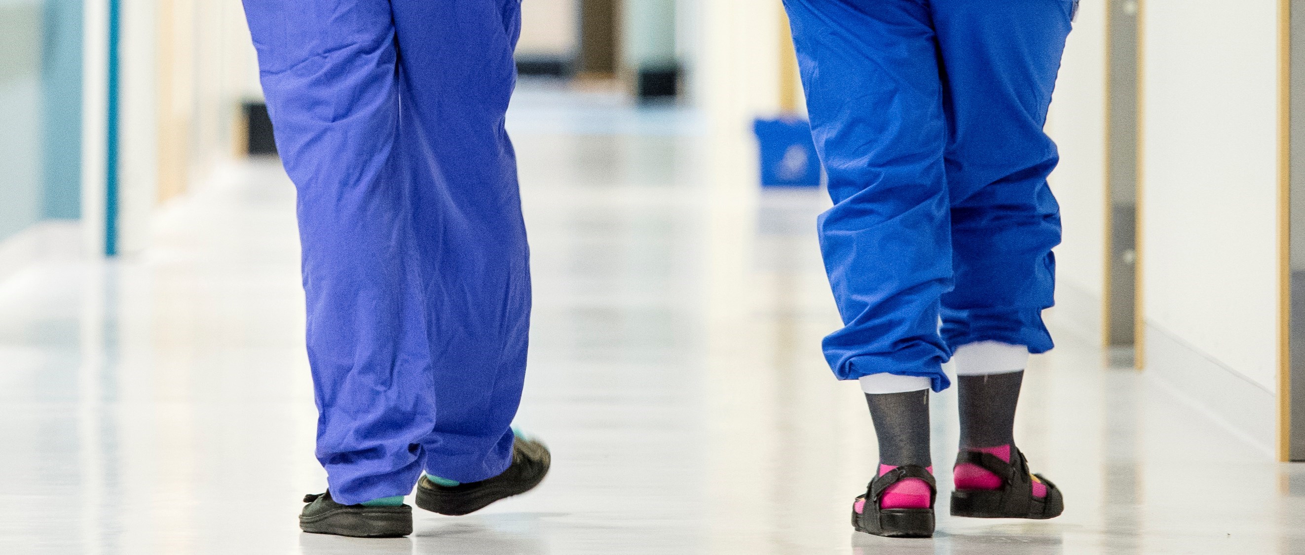 Benen på två hälso- och sjukvårdsarbetare i blå sjukhuskläder går från kameran i en korridor
