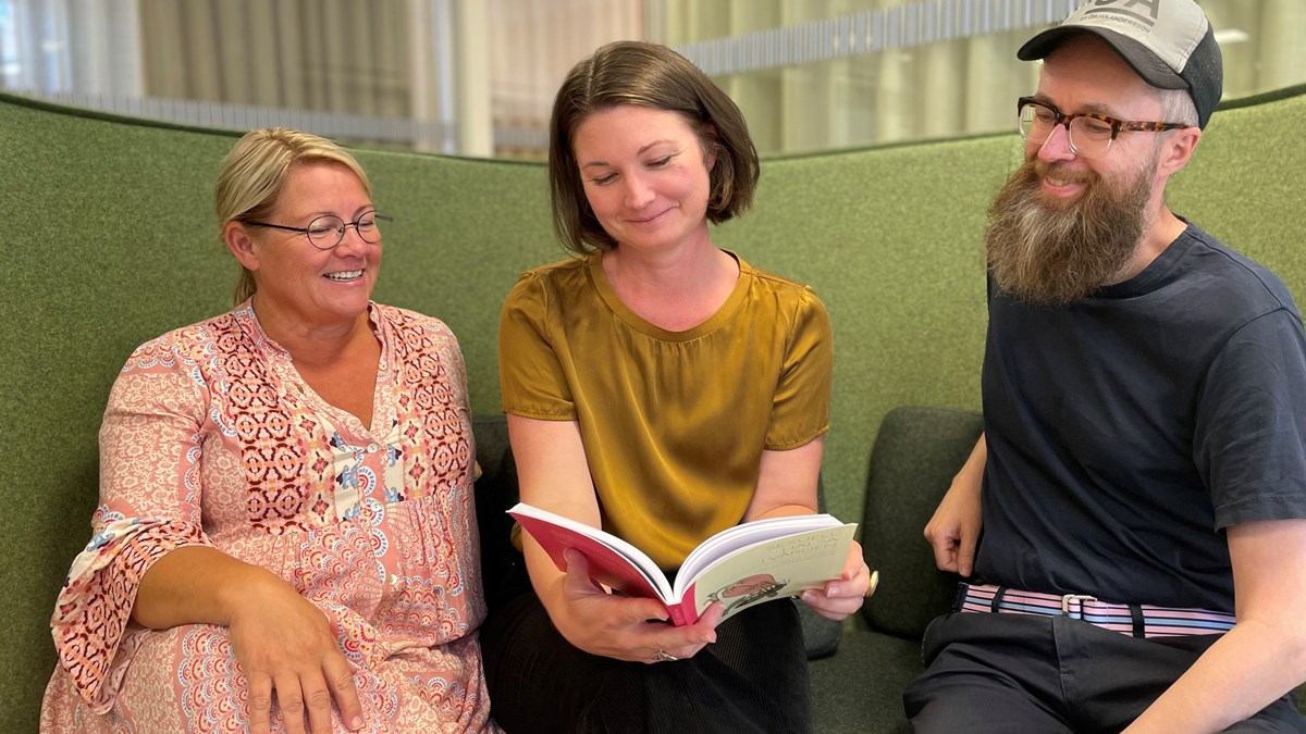 Anna Skoglund, Frida Särén och Per Andreas Persson sitter i en soffa och tittar i kurslitteraturbok.