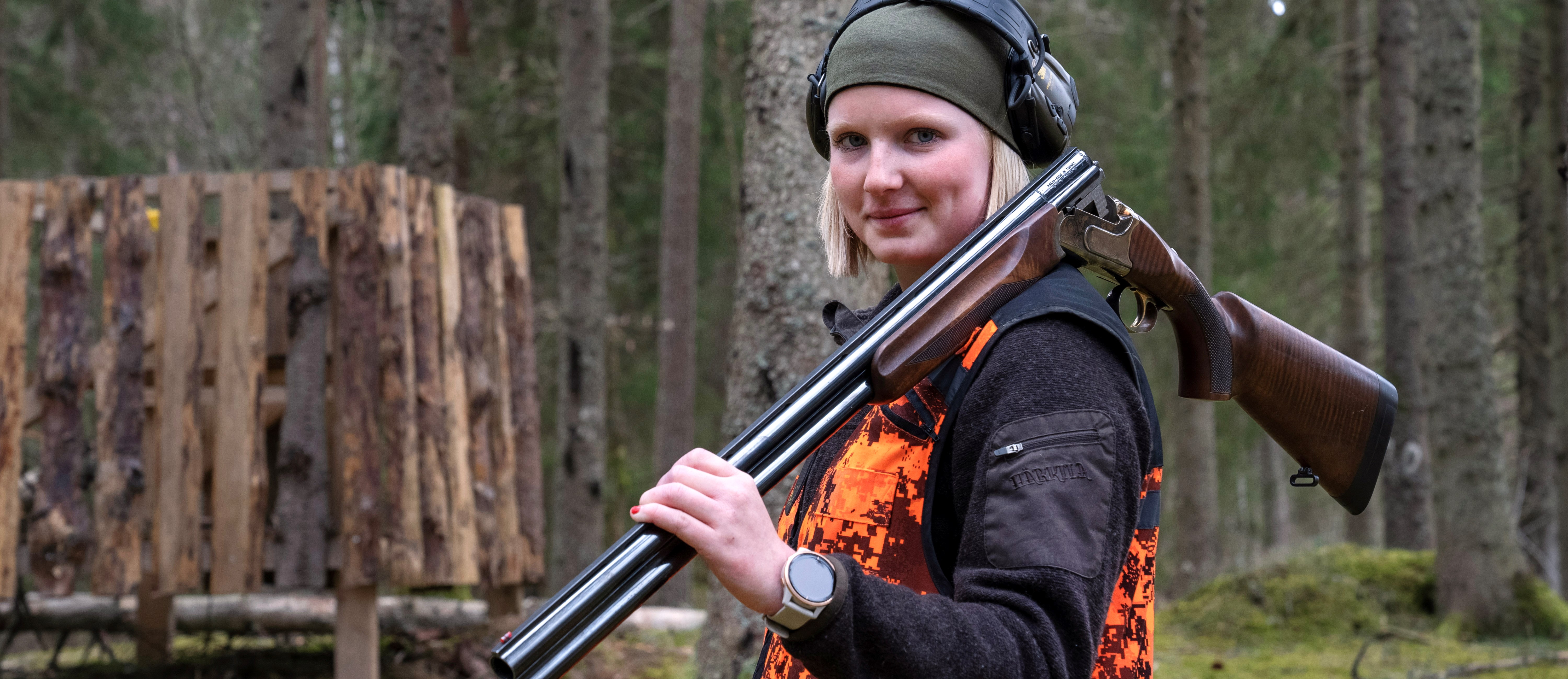 Jaktelev med skyddskläder och hörselskydd står med gevär lutat över axeln
