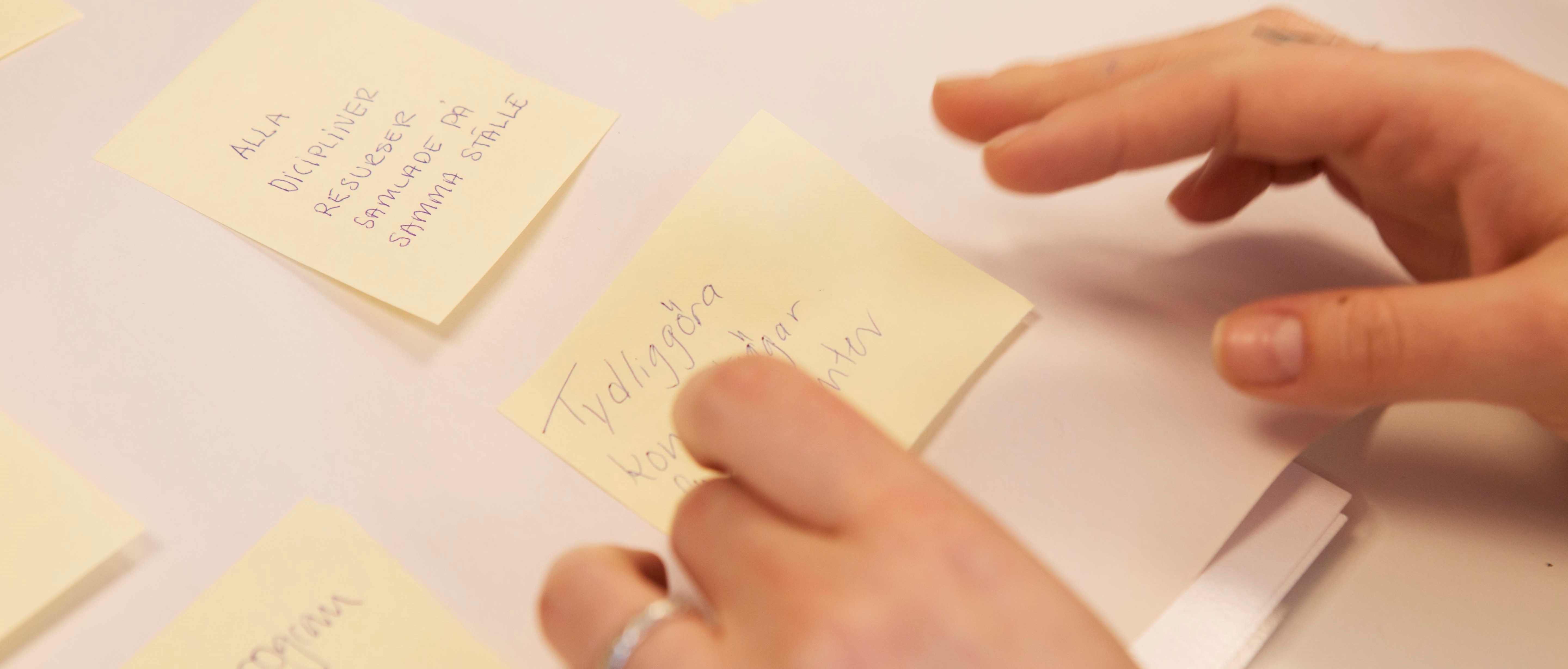 Två händer placerar post it lappar på ett papper