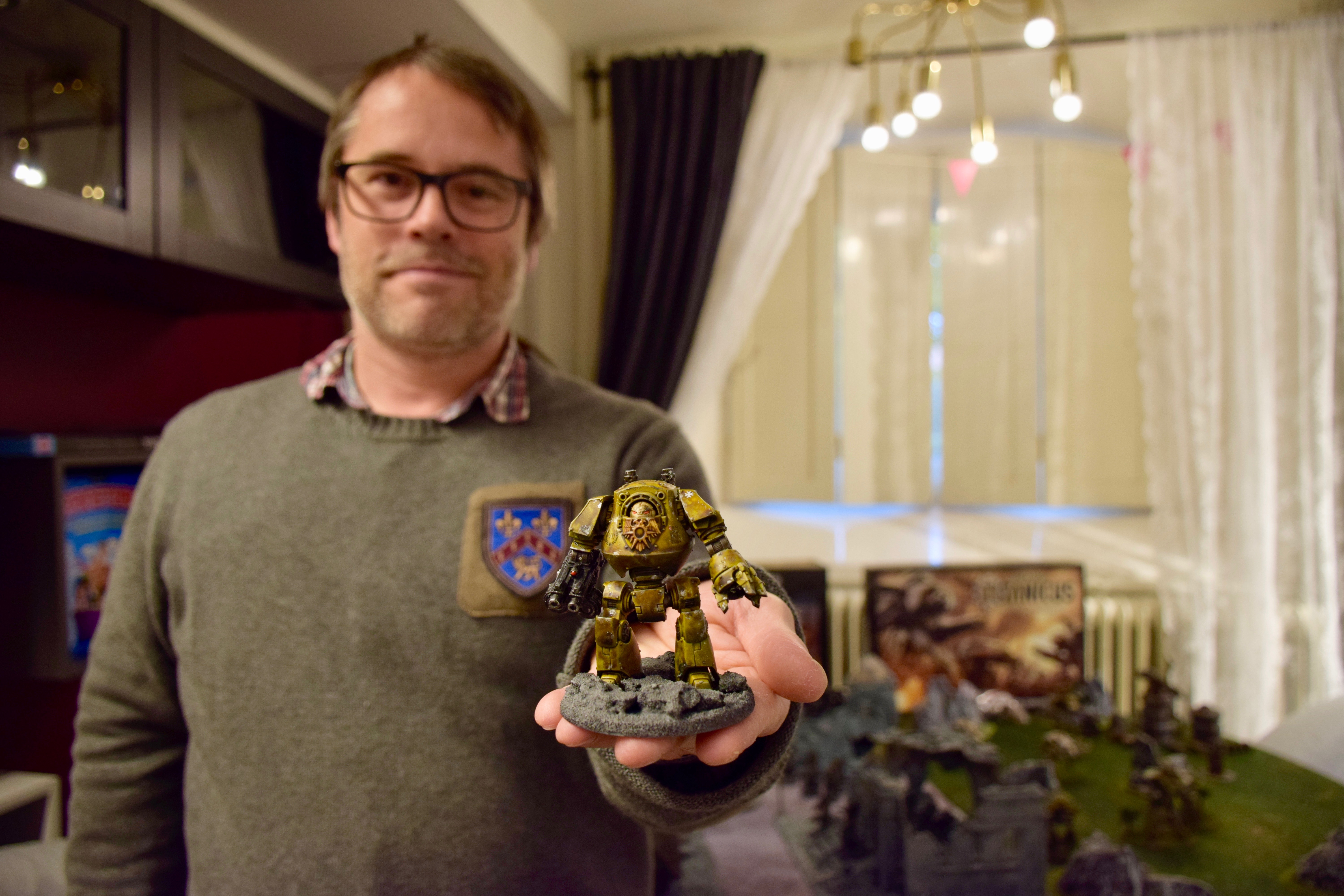 Fredrik Löfqvist håller fram en spelfigur. Fredik är klädd i en grön tröja med ett emblem, han har glasögon och kortklippt brunt hår. 