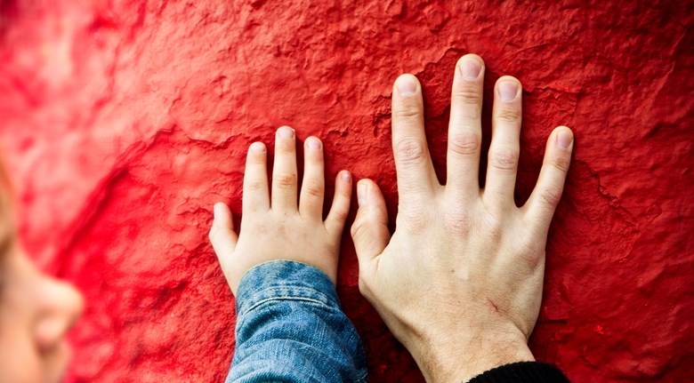En barnhand och en vuxen hand har handlflatan mot en röd stenvägg