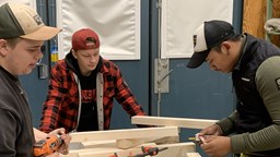 Tre elever bygger tillsammans med trämaterial och olika verktyg
