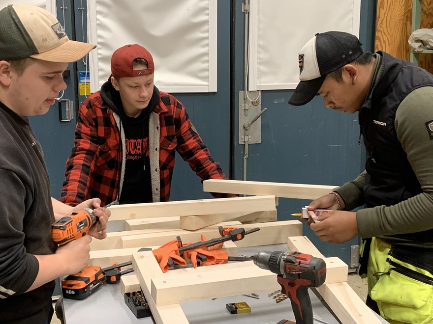 Tre elever bygger tillsammans med trämaterial och olika verktyg