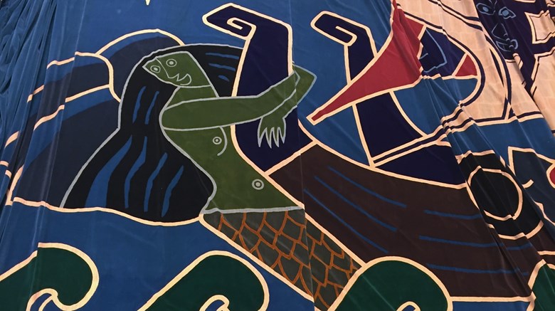 Bilden visar en detalj från biograf Drakens ridå. En stiliserad grön sjöjungfru håller armarna om fören på ett vikingaskepp. Nedanför henne syns stiliserade vågor.