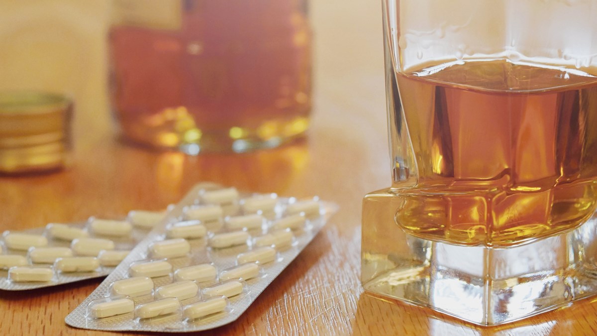 Bilden visar en närbild av ett glas med wiskey och två kartor med tabletter på ett bord.