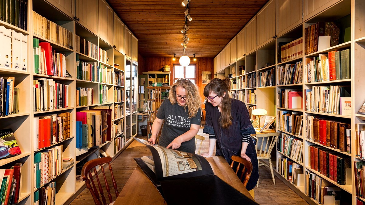 Två personer i ett äldre bibliotek tittar i en stor bok