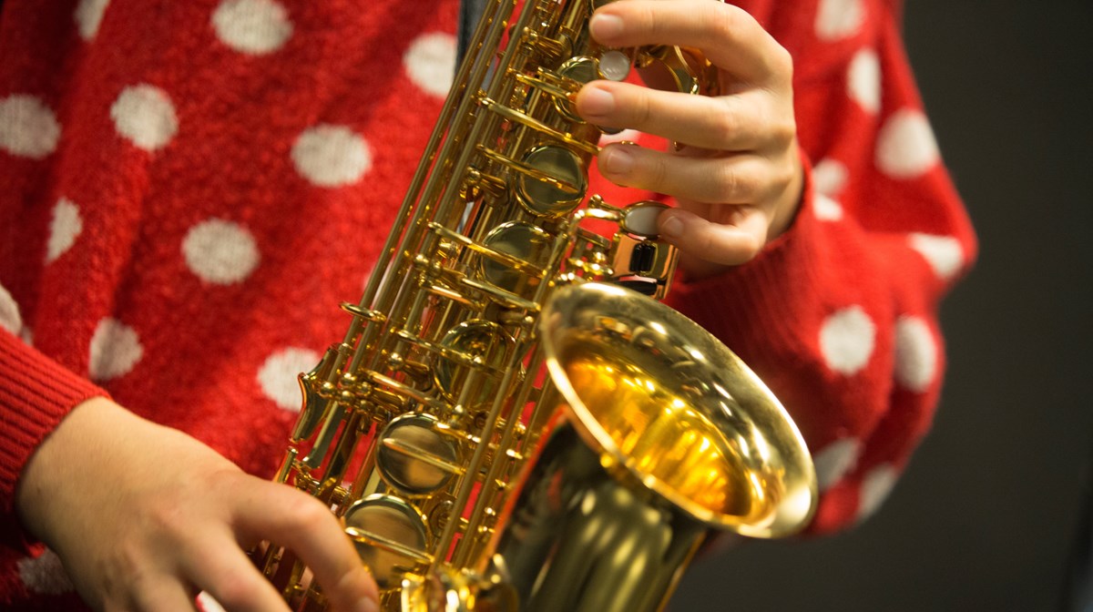 Klockstycket och mittenklaffarna av en saxofon, som en person håller i med två händer. Personen har en röd tröja med vita prickar.