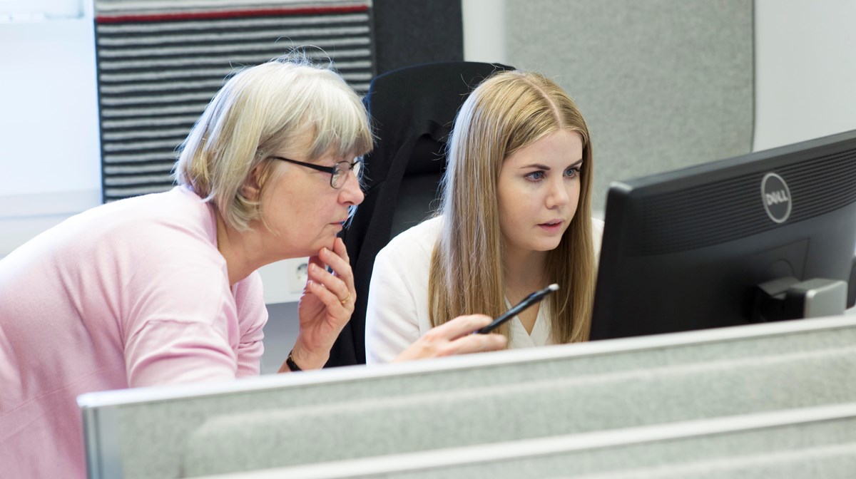 Fotografi taget framifrån. Två kvinnor tittar fokuserat på en datorskärm.