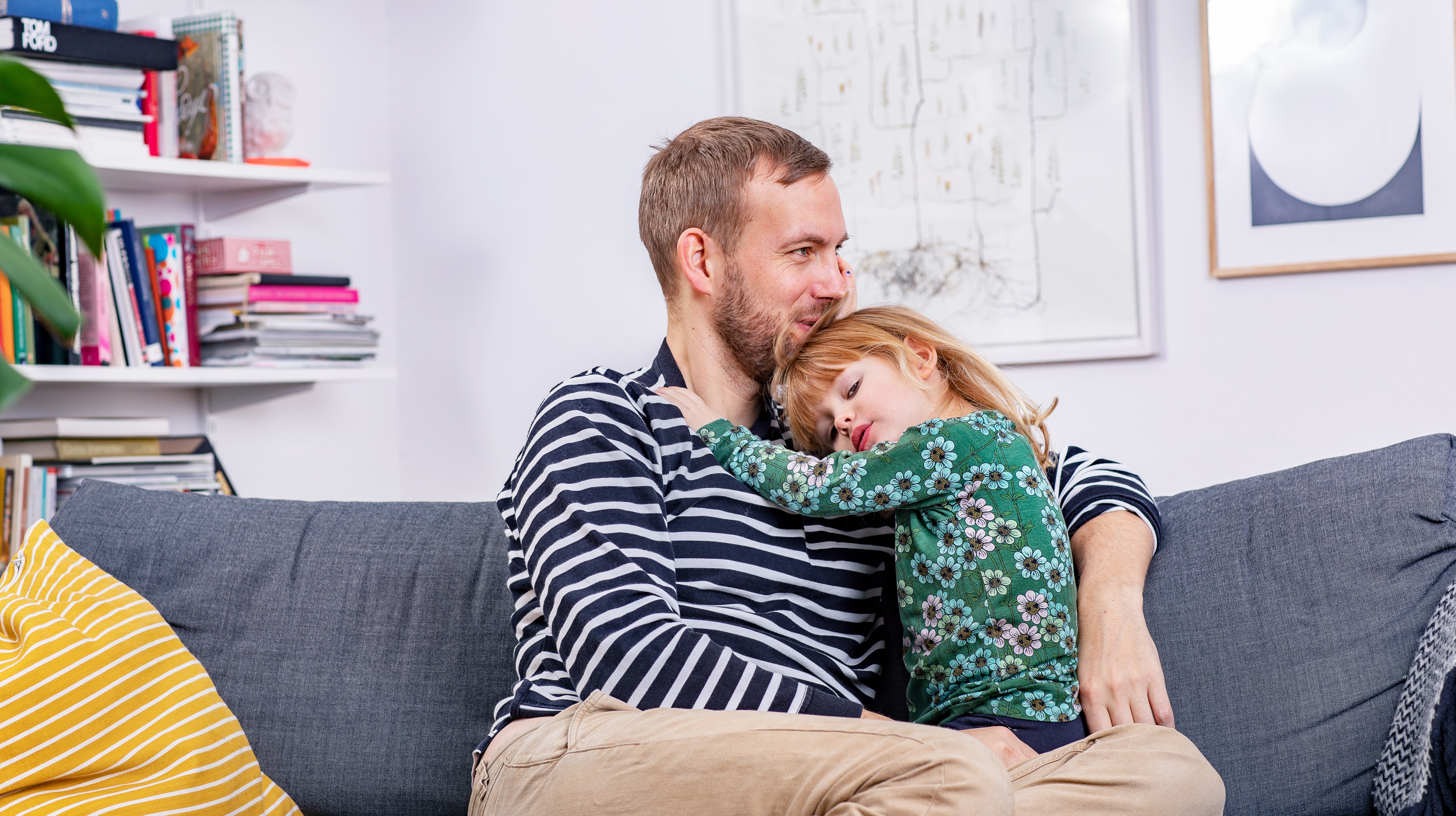 Fotografi taget framfrån. En pappa håller om sitt barn. De sitter i en grå soffa.