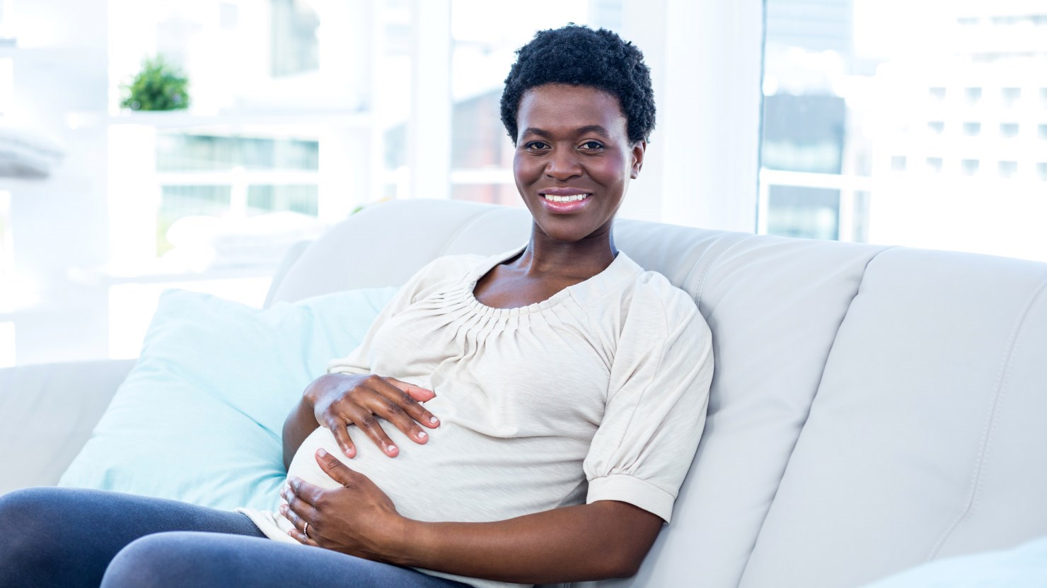 en gravid kvinna sitter i en soffa och håller om sin mage, hon ler och ser lycklig ut