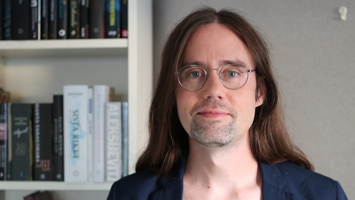 Jon Fällström är i 40-årsåldern. Han har långt brunt hår och runda glasögon. 