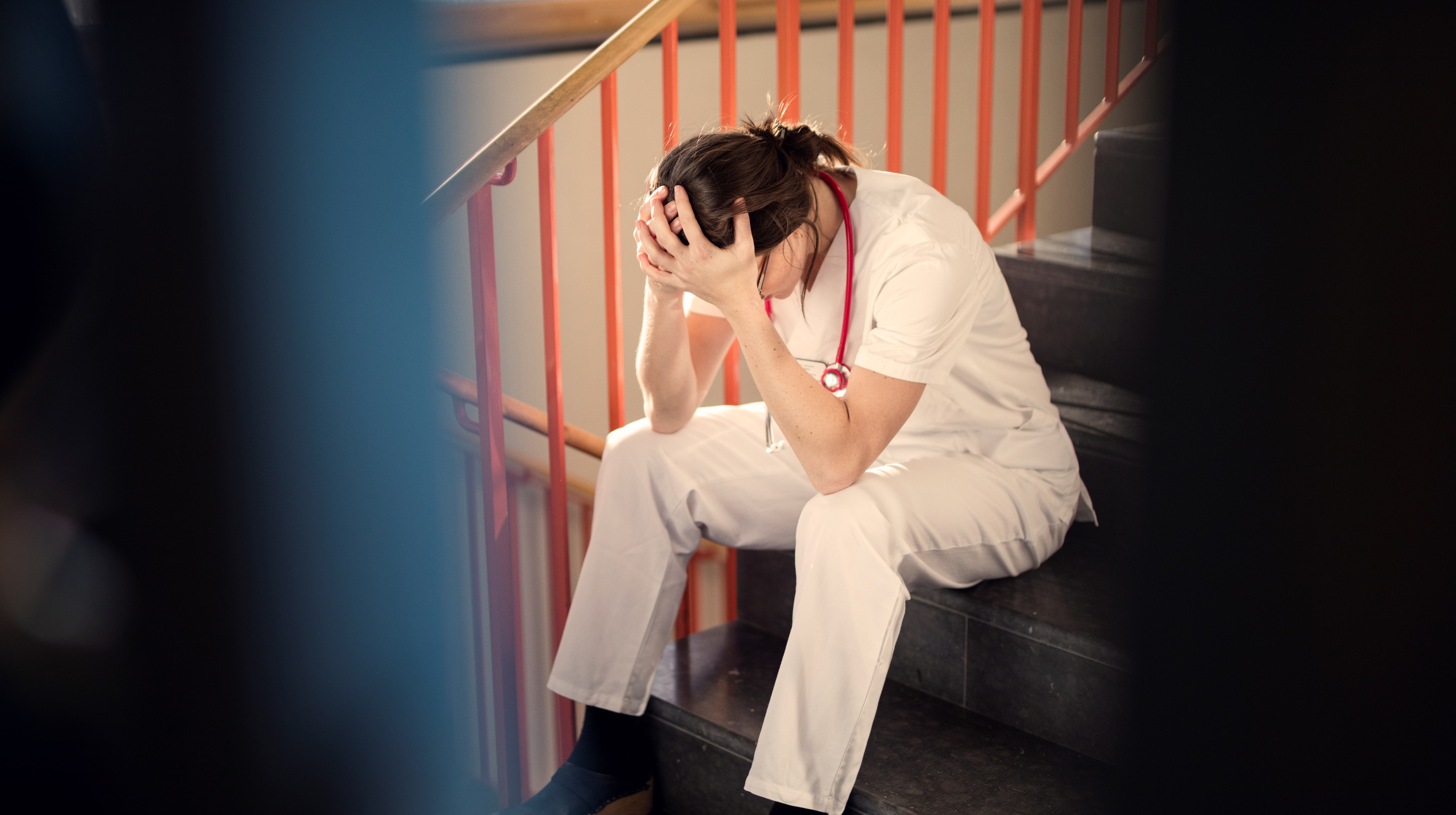 Kvinna som  arbetar i vården sitter utmattad i en trappa