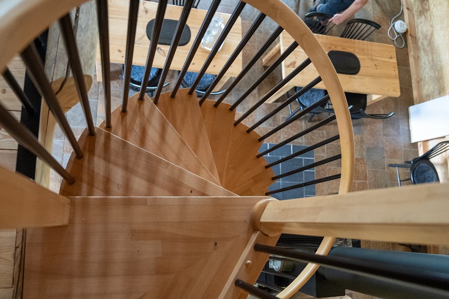 Vy ovanifrån en spiraltrappa i trä där man skymtar nedevåningens bord och stolar