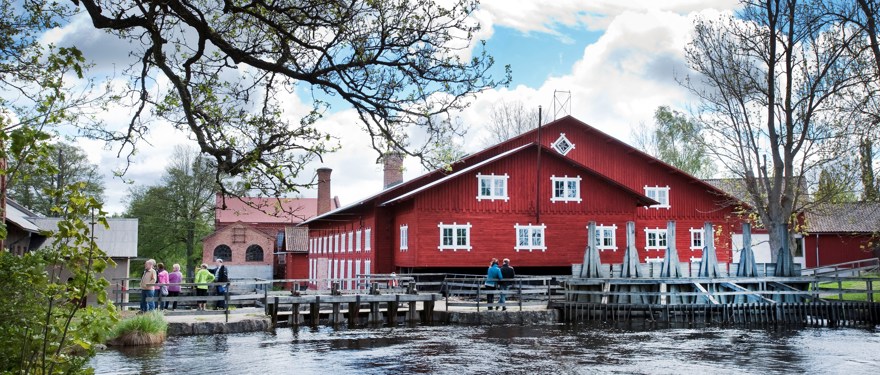 Ett rött hus med vita fönster är byggt nära ett vattendrag