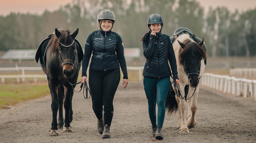 Två elever med ridkläder och hjälm leder varsin islandshäst