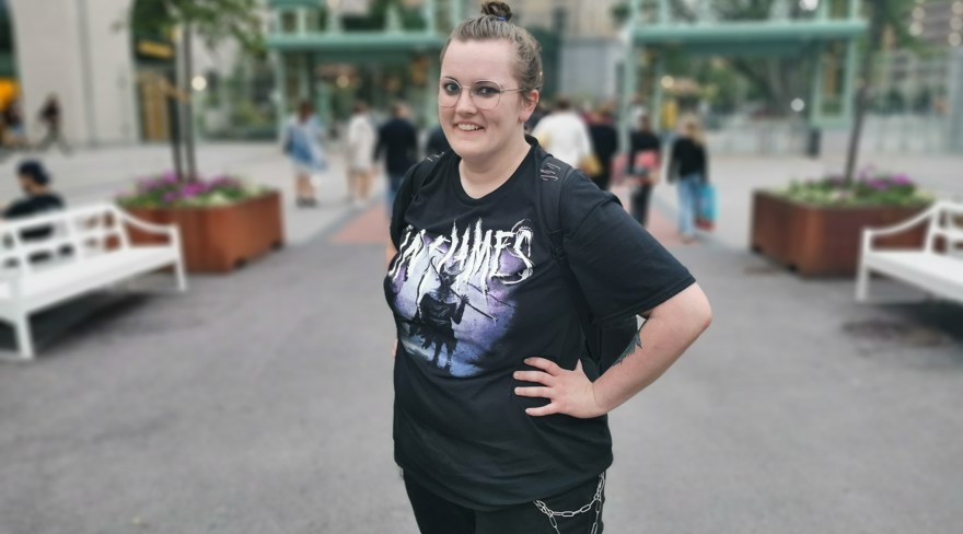 kvinna klädd i svart. InFlames t-shirt. Tofs mitt på huvudet. Glasögon. Kedja som hänger på de svarta jeansen