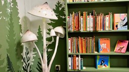 Tre stora vita svampar bredvid en grön bokhylla. 