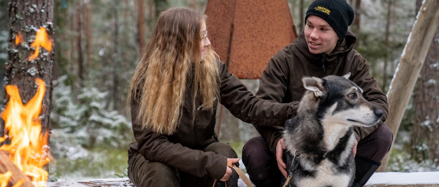 Två elever sitter tillsammans med en hund framför en lägereld