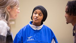 Tre personer inbegripna i ett samtal, i fokus en ung kvinna med blå sportjacka