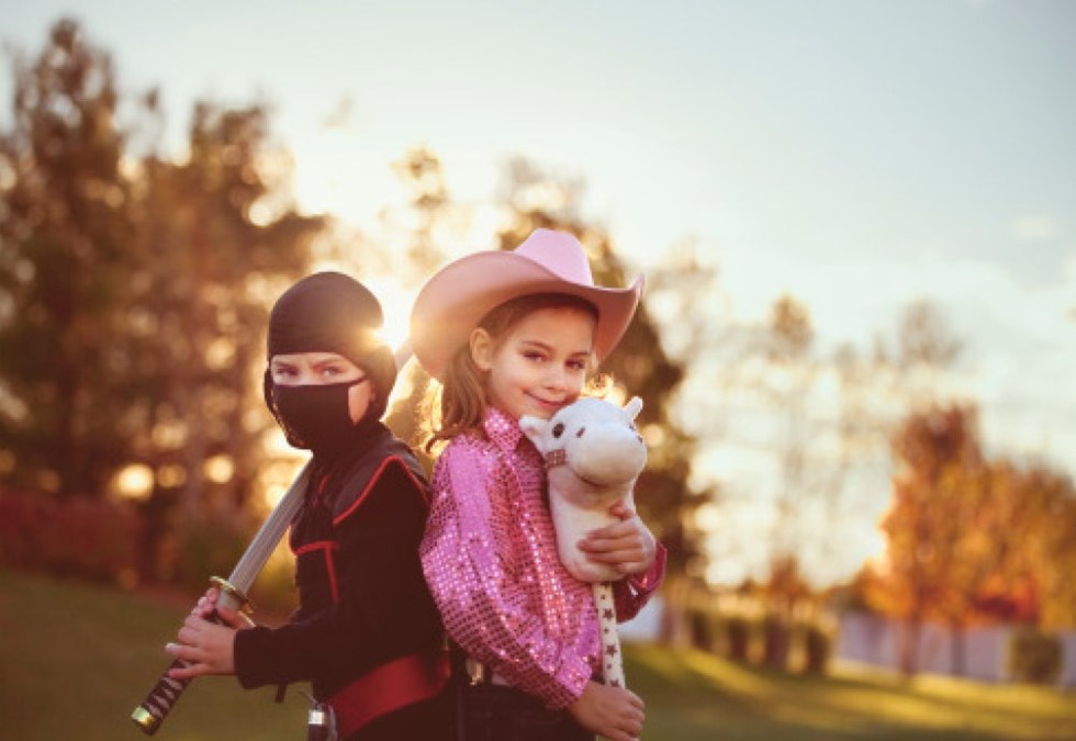 En pojke med bestämd blick, klädd i svart ninjaklädsel och en blygt leende flicka i rosa cowgirlutstyrsel med ett leksaksdjur i famnen.