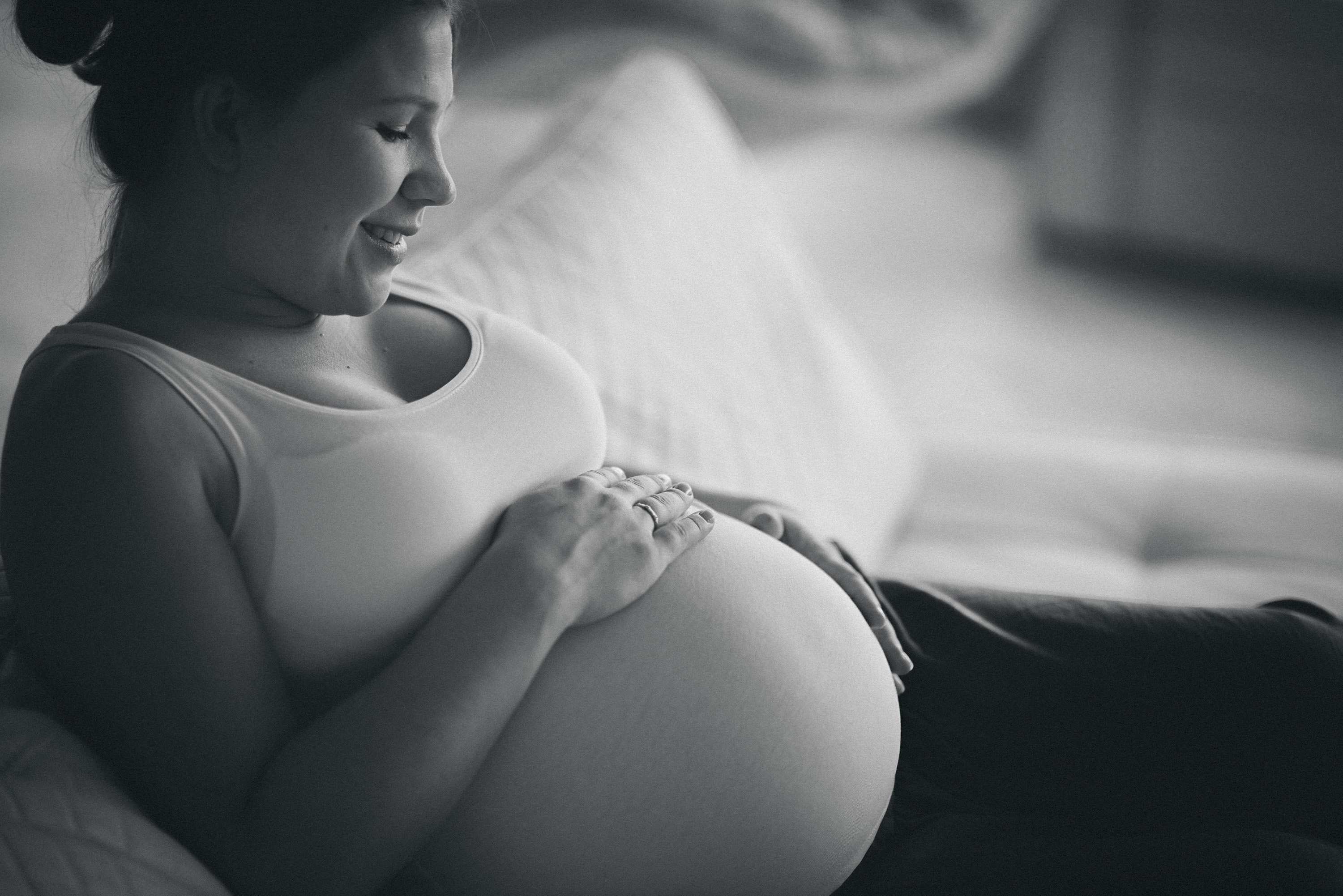 en kvinna med gravid mage håller sina händer på den