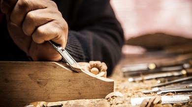 En hand håller i ett verktyg som karvar i ett stycke trä