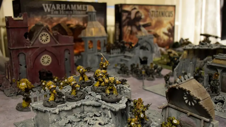 Ett bord med byggnader som tillhör ett spel. Små spelfigurer i plast drabbar samman i förgrunden.