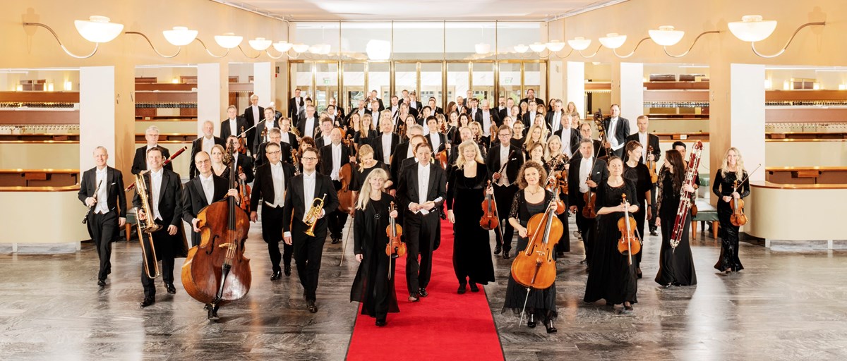 Alla personer som ingår i symfoniorkestern står med sina instrument i en stor hall.