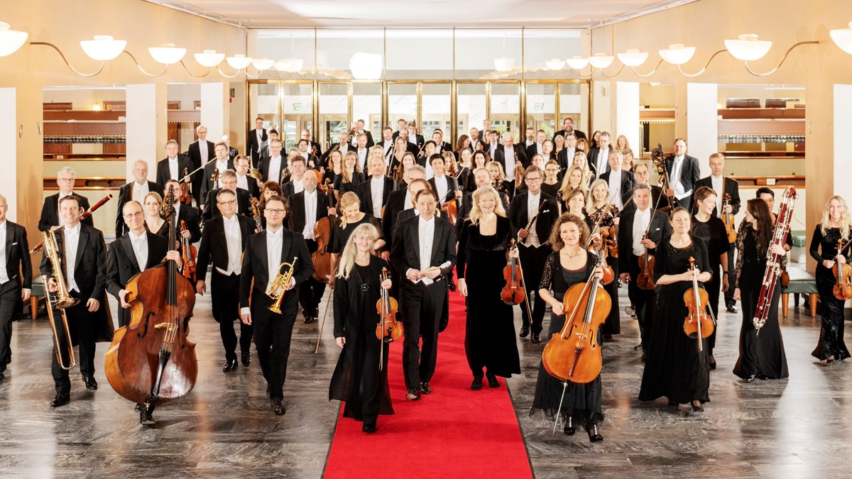 Alla personer som ingår i symfoniorkestern står med sina instrument i en stor hall.