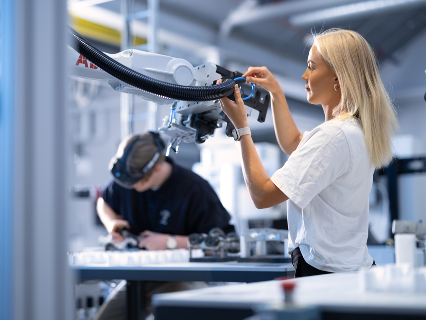 Ung blod kvinna i vit t-shirt står och arbetar med robot.