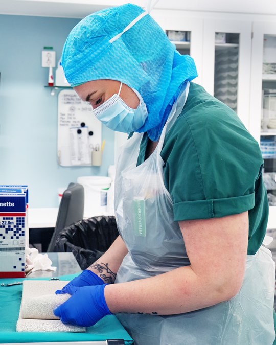 Medarbetare som arbetar i operationssal iklädd blå handskar, munskydd och mössa av papp.
