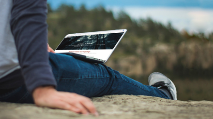 Ett barn sitter på en berghäll med en dator i sitt knä.