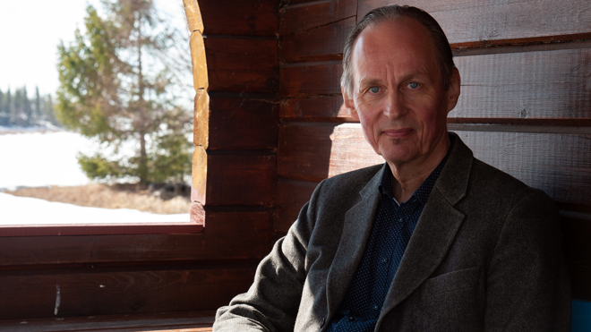 Mikael Niemi är i 65-årsåldern, han sitter inne i en stuga med timrade väggar, alldeles vid ett fönster. Han är klädd i en blå skjorta och en grå kavaj. Hans ögon är blå, håret kortklippt och kammat bakåt och han tittar mot fotografen. Utanför fönstret är det vinter, en stor gran står nära huset, det ligger snö på marken.