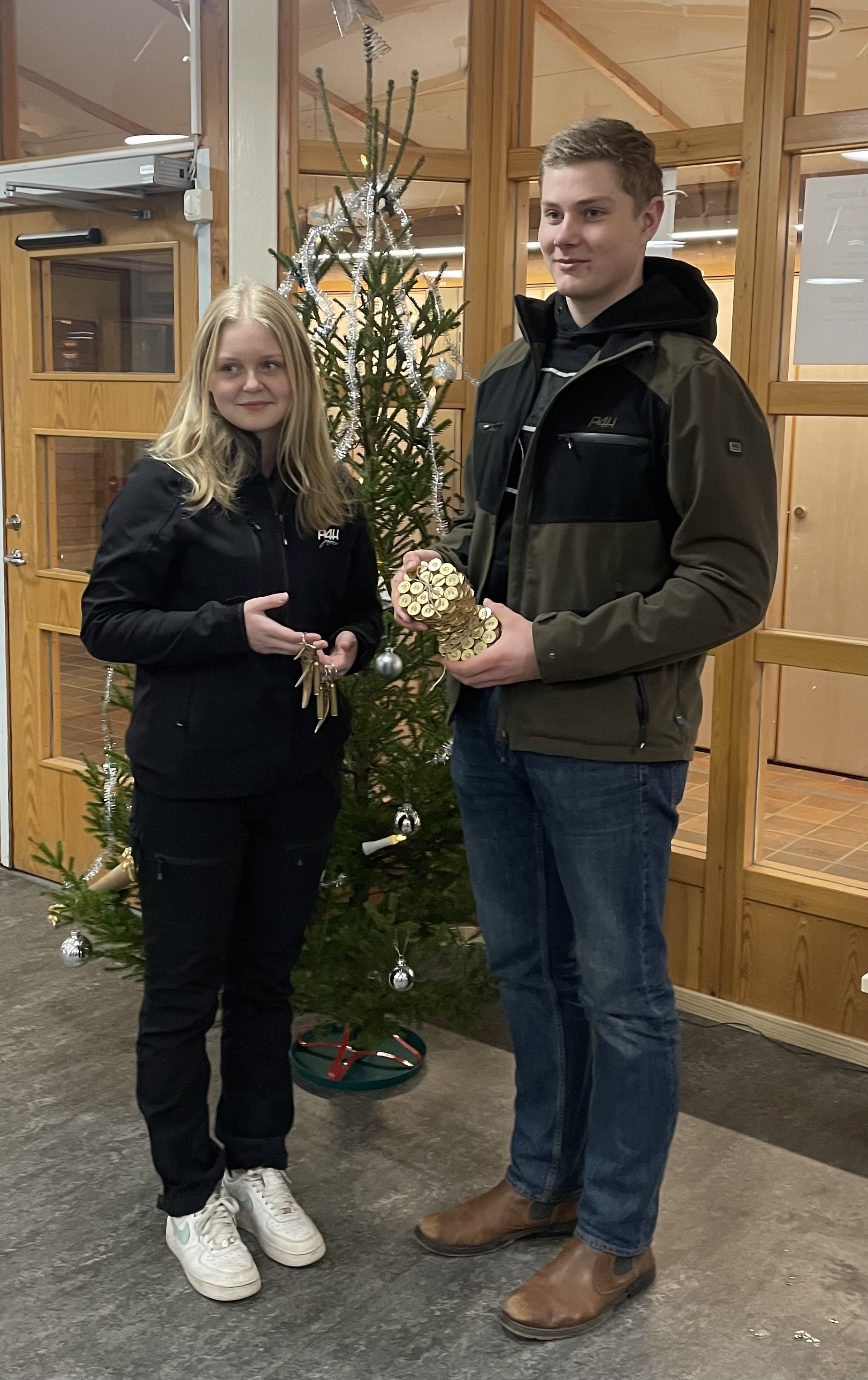 Två elever står framför julgran och håller upp sin UF-produkt