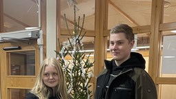 Två elever står framför julgran och håller upp sin UF-produkt
