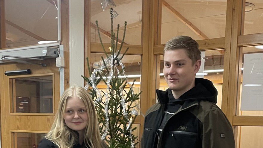 Två elever står framför julgran och håller upp sin UF-produkt