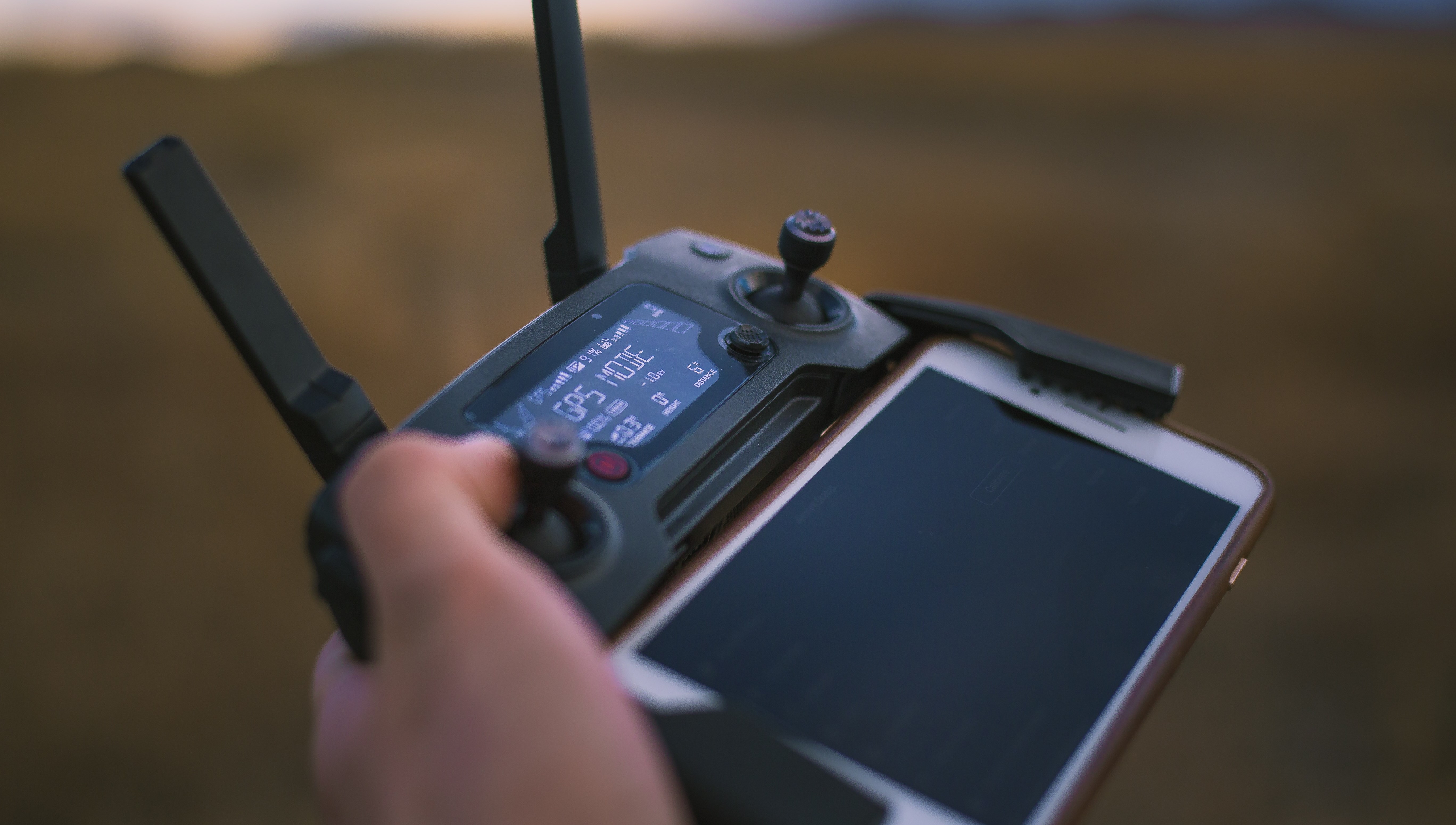 Hand håller i fjärrkontroll till drönare med inkopplad telefon